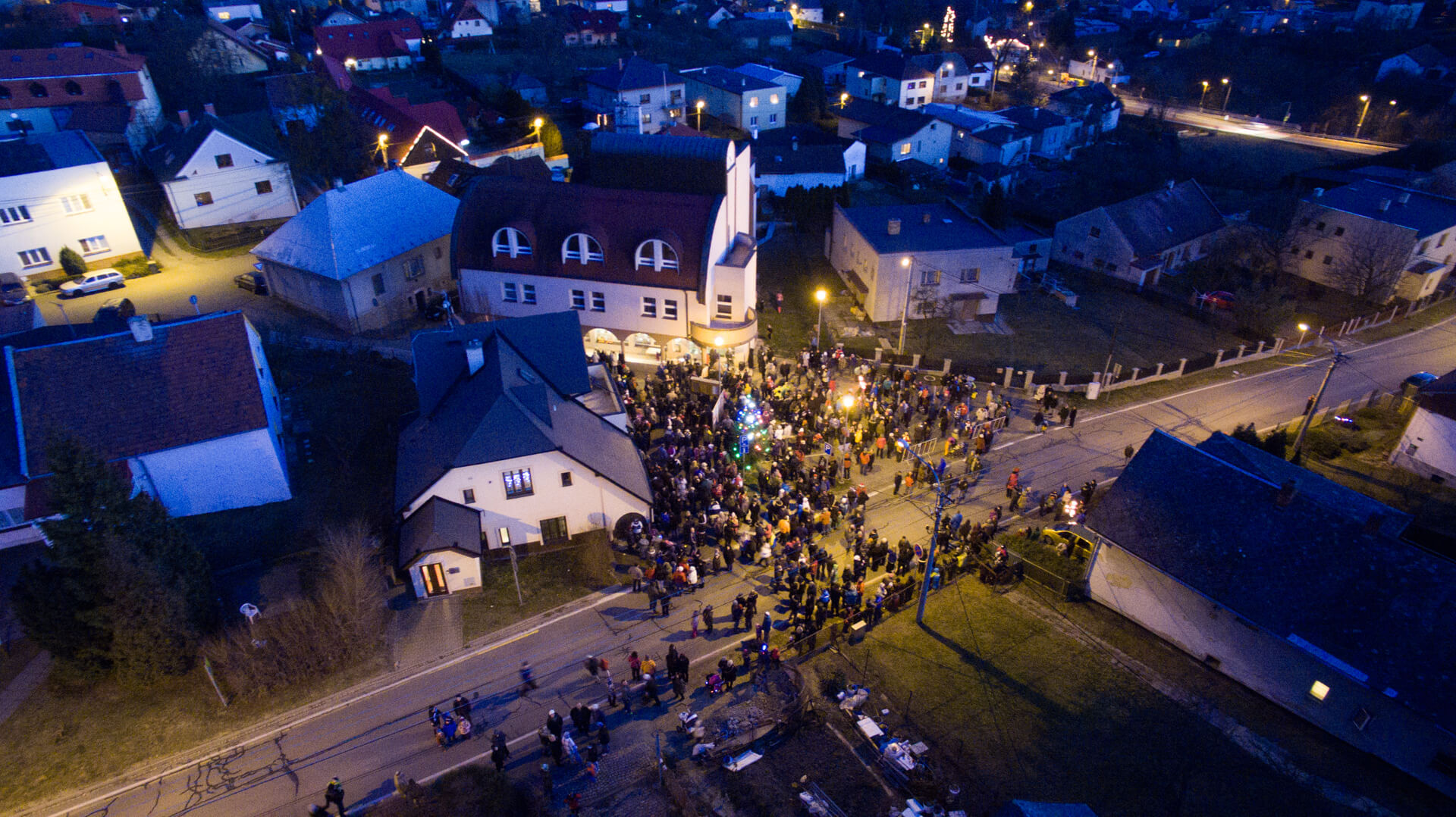 pohled na obec z ptačí perspektivy v noci, shromážděný dav lidí
